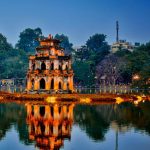 The Turtle Tower is illuminated at night, creating a reflection on the waters of Hoan Kiem Lake in Hanoi.